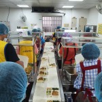 新業(yè)同仁與志工們繫上圍裙、套上防塵帽，戴上口罩，手捧一份份飯包各司其職，為的是準時將熱騰騰的飯包送到長輩手中。