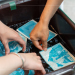 將明信片輕放入水箱中，清洗掉藥水後，隨著雙氧水的洗禮，藍(lán)曬圖像逐漸浮現(xiàn)。